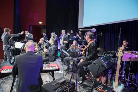 Auf einer Bühne spielt vor einer großen Leinwand ein großes Orchester.