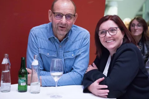 Ein Mann und eine Frau sitzen mit Weingläsern an einem Tisch.