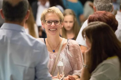 Eine Frau mit Brille lächelt in einer Menschenmenge.