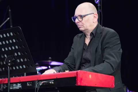 Ein Mann im Anzug spielt auf einer Bühne auf einem roten Keyboard.