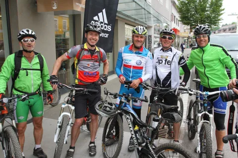 Fünf Radfahrer in bunten Trikots stehen mit ihren Mountainbikes vor dem Geschäft