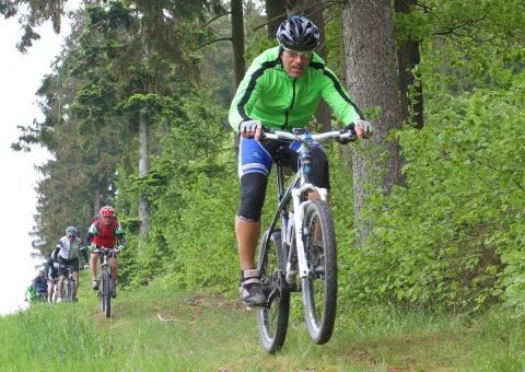 Ein Radfahrer in grüner Jacke fährt durch den Wald, im Hintergrund weitere Teilnehmer