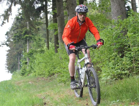 Ein Mountainbiker in orangefarbener Jacke fährt durch den Wald