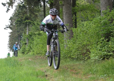 Ein Radfahrer fährt einen steilen Wiesenhang im Wald hinauf