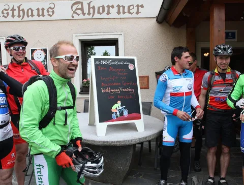 Radfahrer stehen vor dem Gasthaus neben einer beschriebenen Tafel