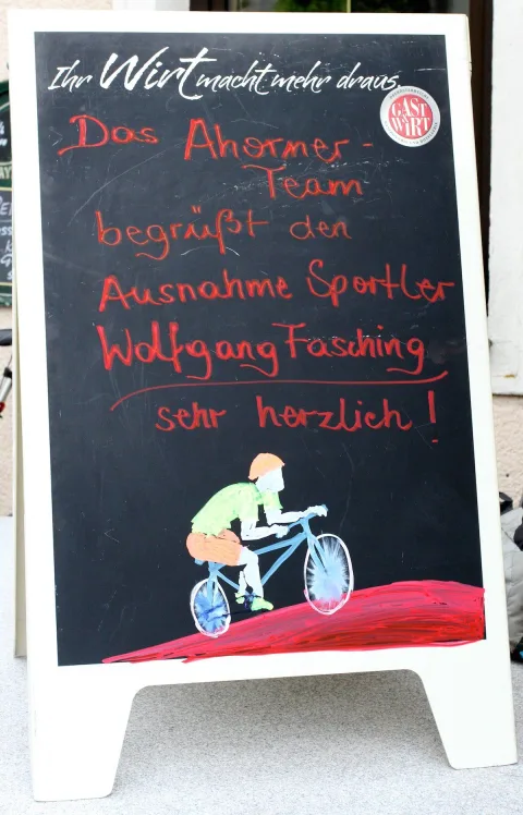 Eine Tafel mit der handgeschriebenen Begrüßung für den Sportler Wolfgang Fasching, mit gemaltem Radfahrer