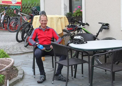Ein Radfahrer sitzt in Radkleidung an einem Gasthaustisch im Freien