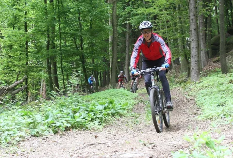 Ein Radfahrer in rotem Trikot fährt über den lehmigen Waldweg