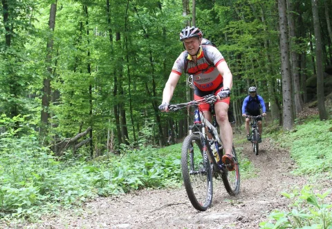 Ein Radfahrer in rot-weißem Trikot fährt durch den Wald, ein weiterer folgt