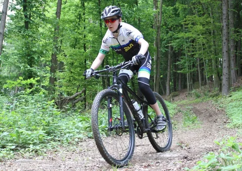 Ein Mountainbiker in dunklem Trikot fährt einen Waldweg entlang