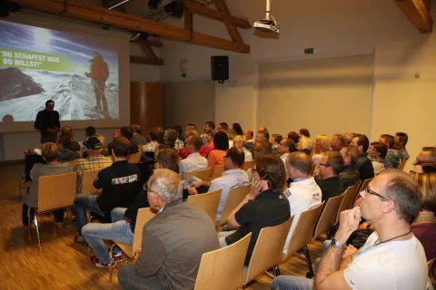 Ein voll besetzter Saal beim Vortrag, das Publikum sitzt in Stuhlreihen