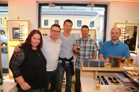 Fünf Personen posieren mit Getränken vor der Brillenwand