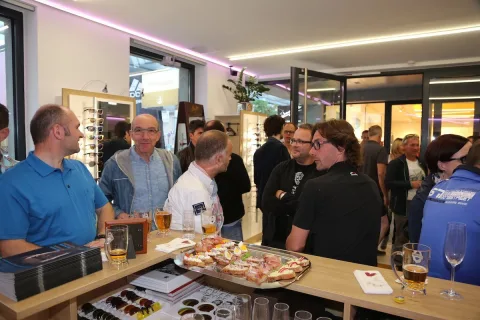 Gäste stehen an einem Buffet mit Pizza und Getränken im Geschäft