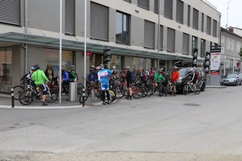 Radfahrer warten mit ihren Rädern an einer Häuserzeile auf den Start