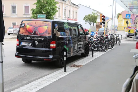 Ein schwarzer Kleinbus mit Aufschrift steht vor der Häuserzeile, dahinter die Räder