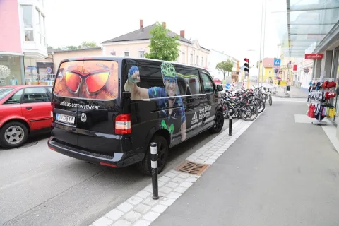 Der beschriftete Kleinbus steht an der Straße, dahinter abgestellte Fahrräder