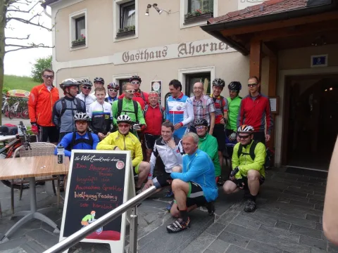 Radfahrer stehen zum Gruppenbild vor dem Gasthaus Ahorner, daneben eine Tafel
