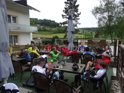 Radfahrer sitzen bei der Rast an Tischen im Gastgarten, Helme liegen auf dem Tisch