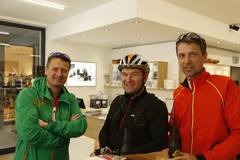 Drei Radfahrer stehen lachend im Geschäft, einer mit verschränkten Armen