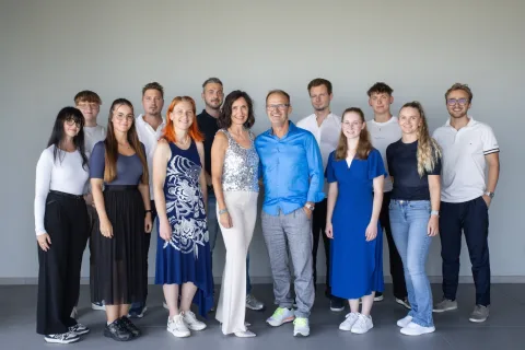 Das Team steht in einer langen Reihe vor einer hellgrauen Wand, rund fünfzehn Personen