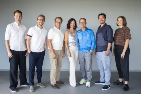 Sieben Personen des Teams stehen nebeneinander vor derselben Wand