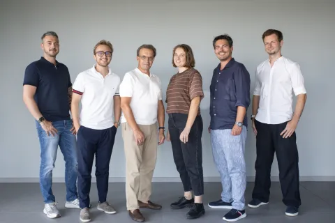 Sechs Personen des Teams stehen nebeneinander vor derselben Wand