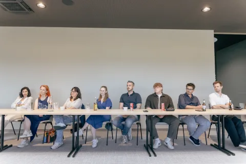 Eine Reihe von Zuhörern sitzt an einem langen Tisch und blickt nach vorne