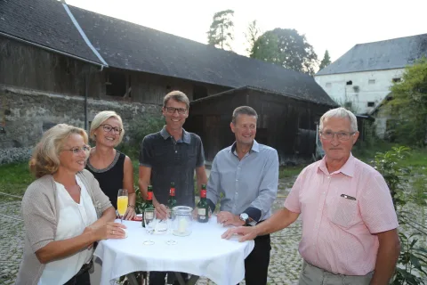 Eine Gruppe von Menschen steht um einen Tisch herum, auf dem Weinflaschen stehen.