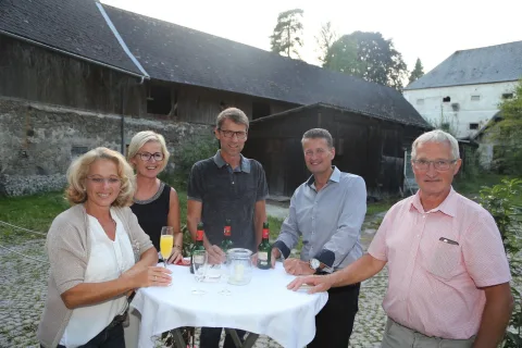 Eine Gruppe von Menschen steht um einen Tisch herum, auf dem Weinflaschen stehen.