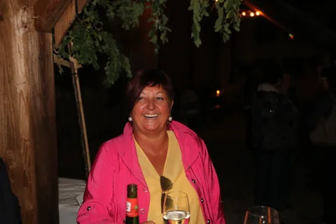 Eine Frau in einer rosa Jacke hält ein Glas Wein.