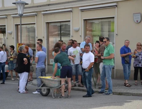 Eine Gruppe von Menschen steht auf einem Bürgersteig, ein Mann schiebt eine Schubkarre