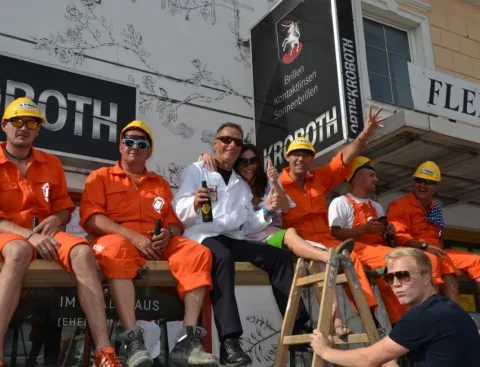 Helfer in orangen Overalls sitzen auf einem Gerüst