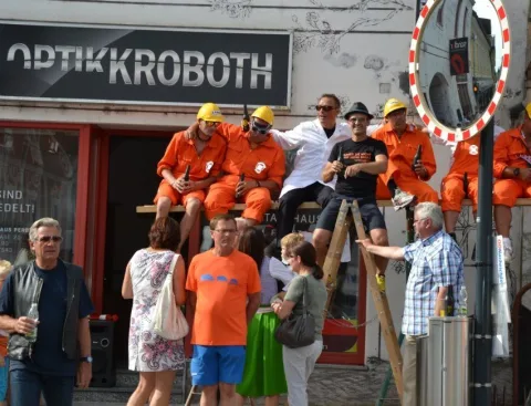 Helfer in orangen Overalls an einer Leiter vor dem Geschäft