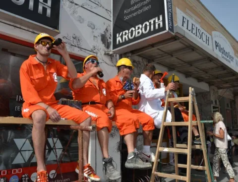 Helfer in orangen Overalls sitzen auf einem Podest