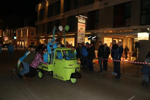 Kinder schieben den Kleintransporter, dahinter Zuschauer